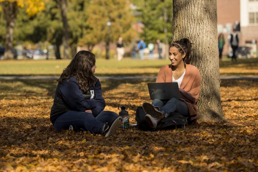 Two students seated on the campus mall in the fall