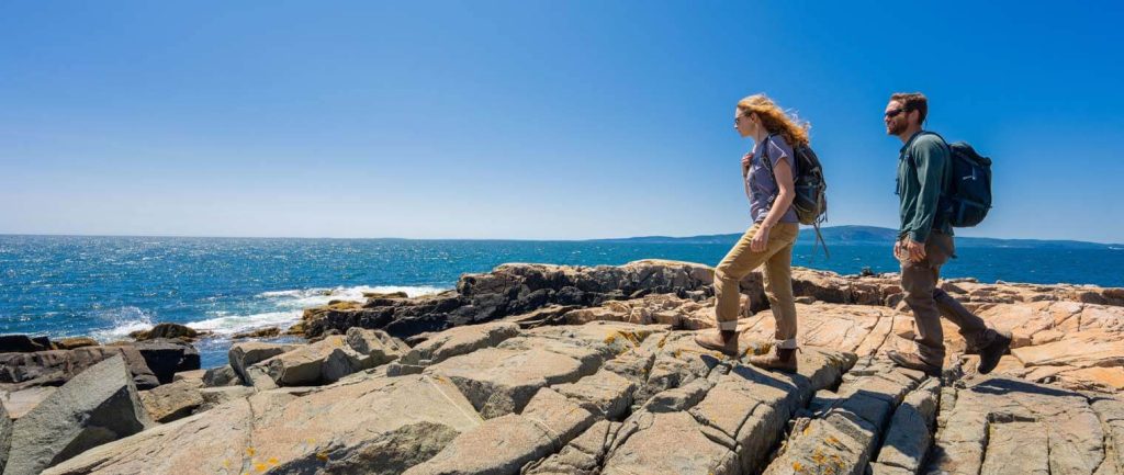 a photo of two people walking on Maine's rocky coast