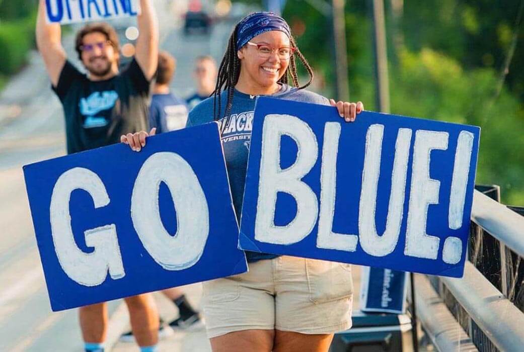 A photo of a student holding signs that say, "Go Blue!"